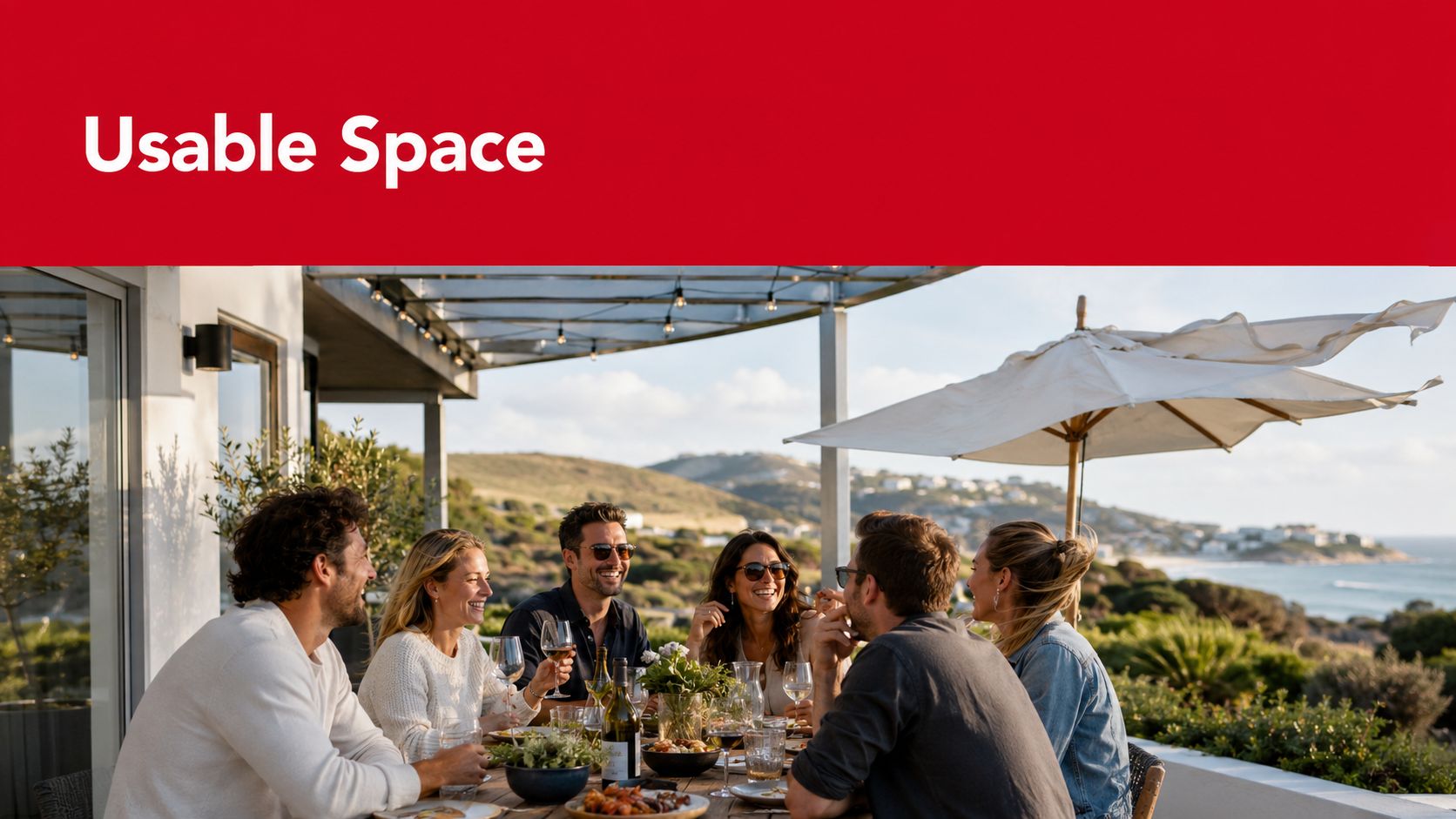A group of friends enjoying a meal and wine at an outdoor patio table overlooking the ocean.